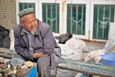 Hotan, Xinjiang, Çin-4 Ekim 2017: Uygur satıcı, Yurungkax nehri yakınlarındaki bir pazarda müşterileri beklerken yeşim taşı ve diğer mineralleri satıyor..