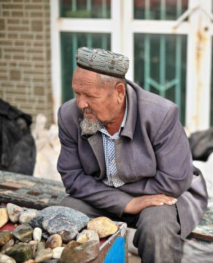 Hotan, Xinjiang, Çin-4 Ekim 2017: Uygur satıcı, Yurungkax nehri yakınlarındaki bir pazarda müşterileri beklerken yeşim taşı ve diğer mineralleri satıyor..