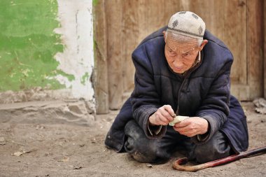 Hotan, Çin-4 Ekim 2017: Uygurlar çoğunlukla Uygur Özerk Bölgesi 'nde yaşayan bir Türk halkıdır. Para sayan tozlu yaşlı dilenci, çakıllı zeminde diz çöker çiftlik hayvanları pazarında.