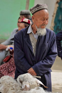 Hotan, Çin-4 Ekim 2017: Uygurlar çoğunlukla Uygur Özerk Bölgesi 'nde yaşayan bir Türk halkıdır. Çiftlik hayvanları pazarında uzun sakallı hayvan terbiyecisi koca kuyruklu koyunlarla..