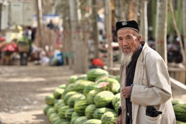 Hotan, Çin-4 Ekim 2017: Uygurlar çoğunlukla Uygur Özerk Bölgesi 'nde yaşayan bir Türk halkıdır. Düşünceli, beyaz sakallı yaşlı bir adam çiftlik hayvanları pazarındaki karpuz standına gelir..