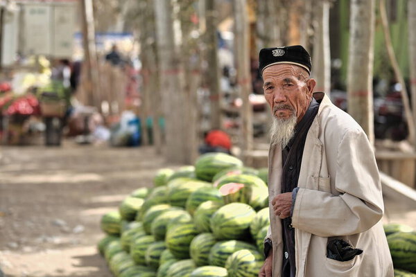 Hotan, China-October 4, 2017: Uyghurs are a Turkic people living mainly in the Xinjiang Uyghur Autonomous region. Thoughtful white-bearded old man comes to a watermelon stand in the Livestock Market.
