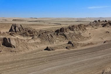 NW-SE, Nal yakınlarındaki rüzgâr erozyonuyla tektonik olarak katlanmış tortu kayalarına oyulmuş, yarda uzunluklu arazi şekillerinin hizalanması. Qaidam havzası çölünü geçen G315 karayolu. Qinghai Eyaleti-Çin.