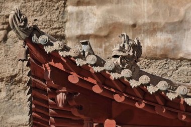 Upturned eaves on tiled roof with dragon figures-9 story high wooden porch of cave 96-Mogao Caves S.area with 492 caves and cell temples dating from centuries 4th to 14th. Dunhuang-Gansu prov.-China. clipart