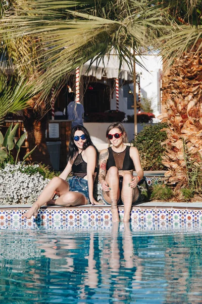 Schöne junge Frauen mit Sonnenbrille lächeln in die Kamera, während sie sich in der Nähe des Swimmingpools im Resort in Ägypten ausruhen — Stockfoto