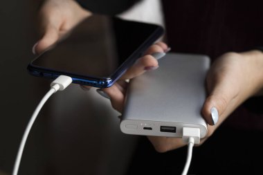 İki kızın elleri telefon ve şarj aletini tutuyor. Powerbank ve akıllı telefon kızların elinde. Enerji şarj aleti, banka akıllı telefonu. Ücret paylaşımı.