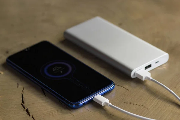 Smartphone-Laden mit Powerbank auf Holztisch. Gebührenanteil Stockbild