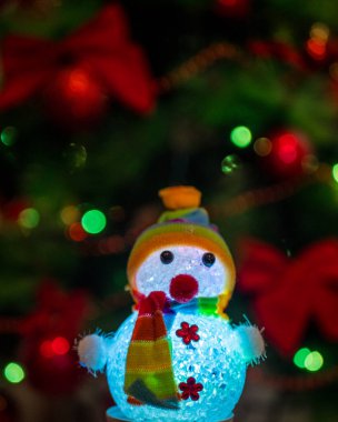 Noel ağacı arka planında çelenklerle parlayan kardan adam