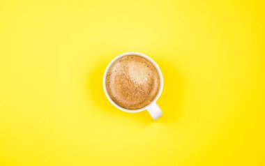 Sarı arkaplandaki kahve fincanının üst görüntüsü. Düz yatıyordu. Boşluğu kopyala