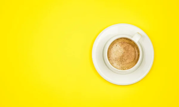 Sarı arkaplandaki kahve fincanının üst görüntüsü. Düz yatıyordu. Boşluğu kopyala