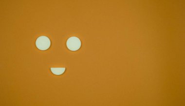 Sarı arka planda beyaz yuvarlak haplar ve gülen surat şeklinde kopyalama alanı.