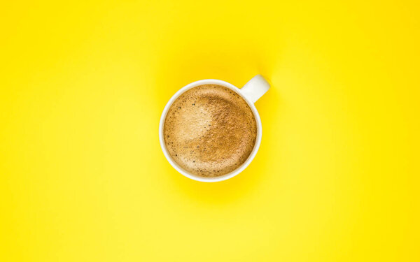 A cup of black coffee on yellow background. View from above. copy space