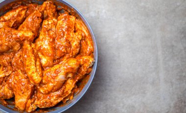 Terbiye edilmiş tavuk kanatları, gri arka planda bir tabakta.