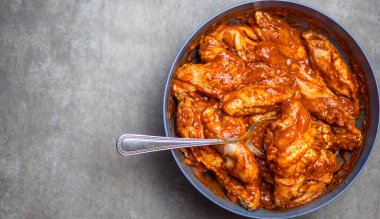 Terbiye edilmiş tavuk kanatları, gri arka planda bir tabakta.