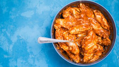 Mavi arka planda bir tabakta marine edilmiş tavuk kanatları. Boşluğu kopyala