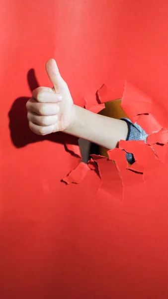 Mão da criança com buraco fundo vermelho, segura o dedo para cima — Fotografia de Stock