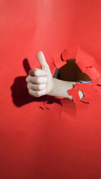 Mano del niño con el fondo rojo agujero, sostiene el dedo hacia arriba — Foto de Stock