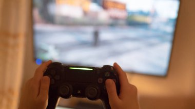 Video oyunu oynayan adam. Eller konsol kontrolörünü tutuyor. Televizyonda futbol ya da futbol maçı. Geniş ekran televizyon klozetin üzerinde duruyor