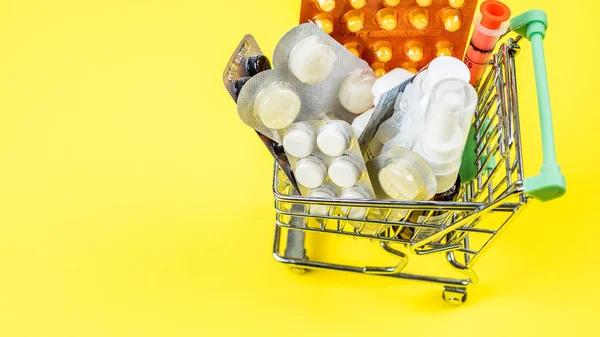 Carro de la compra con ampollas de píldoras de cápsulas médicas sobre fondo amarillo — Foto de Stock