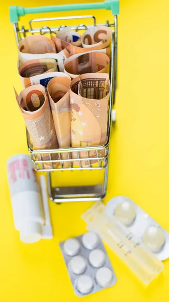 Carrinho de compras com pílulas de medicina em dinheiro - Conceito de custo farmacêutico — Fotografia de Stock