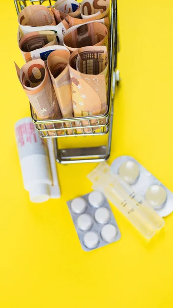 Carrinho de compras cheio de medicamentos com comprimidos e cápsulas e notas de euro. Dinheiro. conceito de custo da droga — Fotografia de Stock