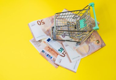 Süpermarket arabası sarı arka planda Avro parasının üzerinde duruyor