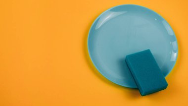 Turuncu arka planda yeşil bir tabakta temizlik süngeri.