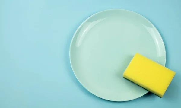 Washing dishes concept. Plate with a sponge on a blue pastel background, Top view — 图库照片