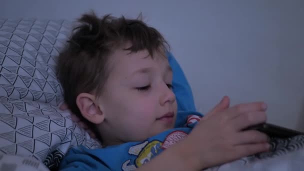 Klein kind spelen smartphone liggend op bed — Stockvideo