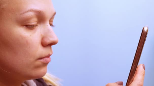 Mujer mirando el teléfono de cerca, sobre un fondo azul — Vídeos de Stock