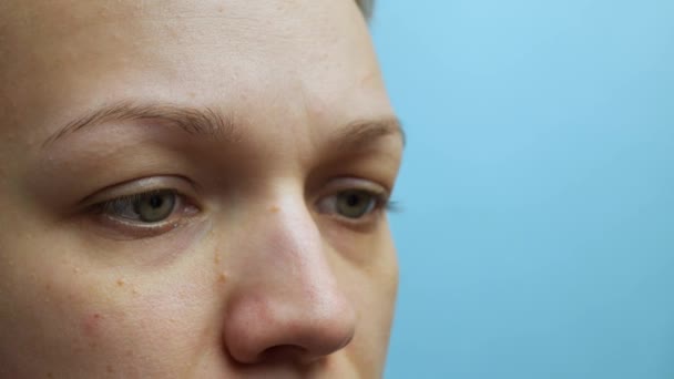 Los ojos de una joven parpadea en cámara lenta sobre un fondo azul. Hermoso ojo azul femenino de cerca. cara femenina de cerca, sobre fondo azul — Vídeos de Stock