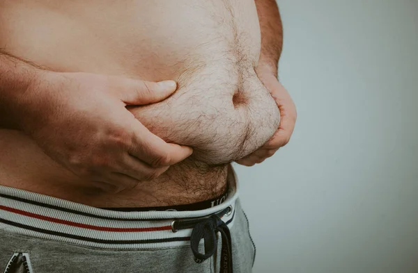 overweight mans hand holds excess belly fat