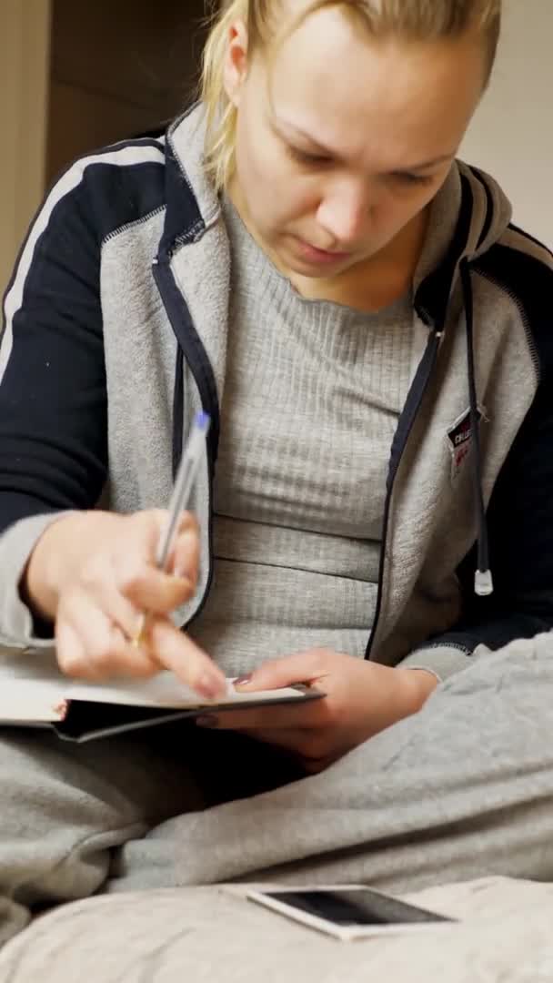 Studentin schreibt in Notizen, Fernstudium. auf dem Bett sitzend. vertikales Video — Stockvideo