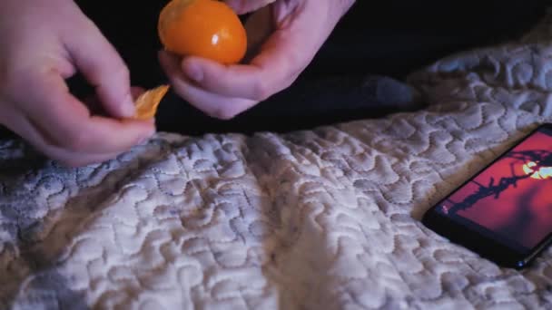 Man clementin peeling op bed en kijken naar de telefoon — Stockvideo