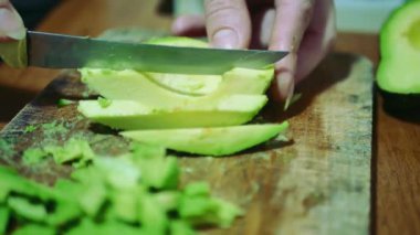 Bir kadının ahşap bir kesme tahtasıyla avokado keserken yakın plan fotoğrafı.