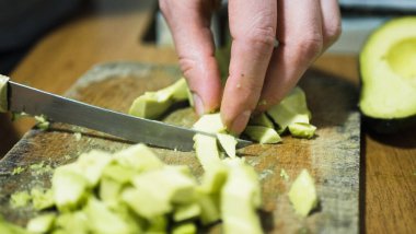 Kadın elleri güvertede avokado kesiyor, dilimlenmiş ve tüm avokado kasesi ahşap arka planda. ev yemekleri.