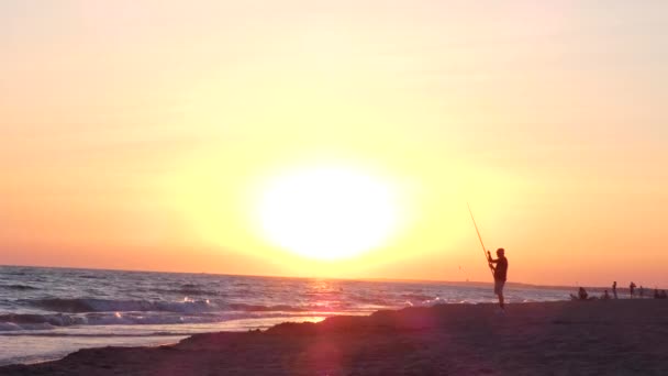 Nerozpoznatelný silueta rybář rybaření na pláži západ slunce. filmový záběr steadicamu — Stock video