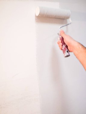 İnşaatçı boyacı bir silindirle duvarı boyuyor..