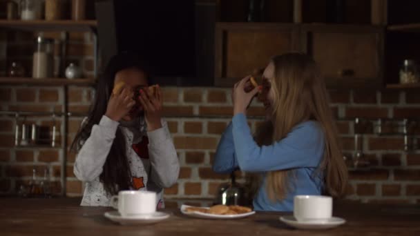 Grappige meisjes die betrekking hebben op ogen met cookies in de keuken — Stockvideo