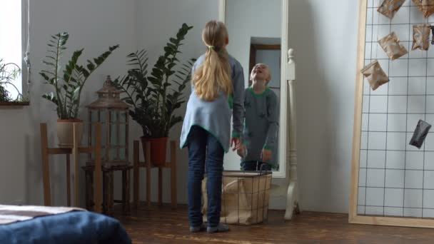 Беззаботная маленькая девочка строит смешные рожи в зеркале — стоковое видео
