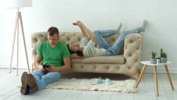 Casal usando dispositivos digitais no sofá acolhedor em casa — Vídeo de Stock