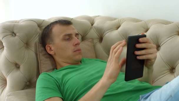 Gioioso uomo websurfing con tablet pc sul divano — Video Stock