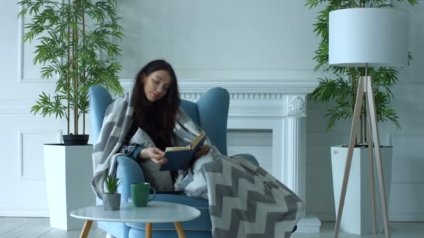 Pretty woman reading a book in armchair at home — Stock Video