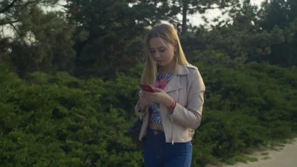 Mujer encantadora caminando y utilizando el teléfono celular en el parque — Vídeos de Stock