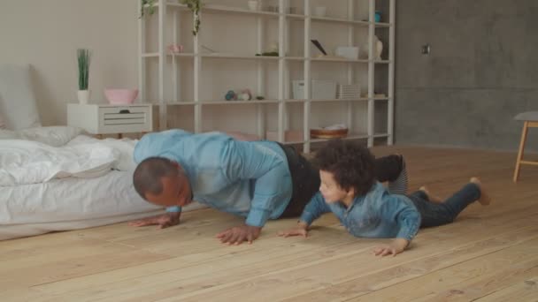 Papá e hijo despreocupados haciendo flexiones en casa — Vídeos de Stock