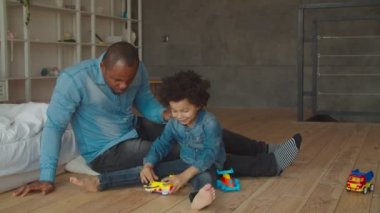 Afrikalı baba ve oğul yerde oyuncaklarla oynuyorlar.