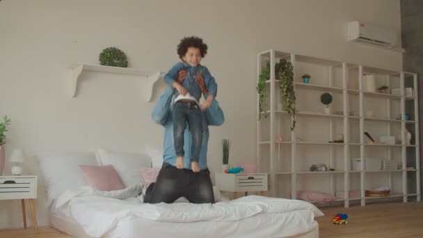 Freudiger schwarzer Vater und kleiner Sohn springen auf Bett — Stockvideo