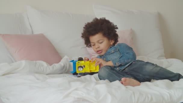 Leuke gemengde ras jongen spelen met speelgoed auto op bed — Stockvideo