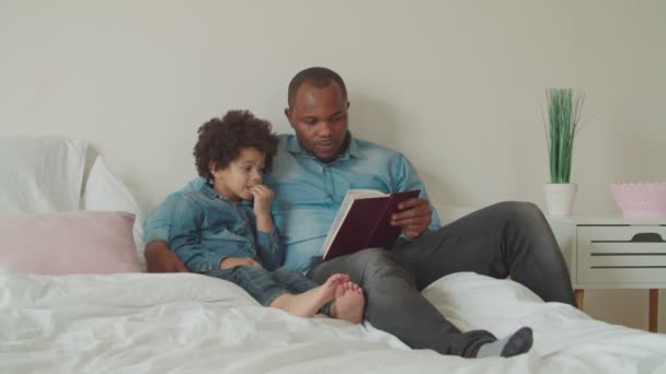 Χαρούμενη ποικιλόμορφη οικογένεια διαβάζοντας ένα βιβλίο που βρίσκεται στο κρεβάτι — Αρχείο Βίντεο