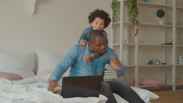 Hijo juguetón abrazando ocupado papá negro en el dormitorio — Vídeo de stock